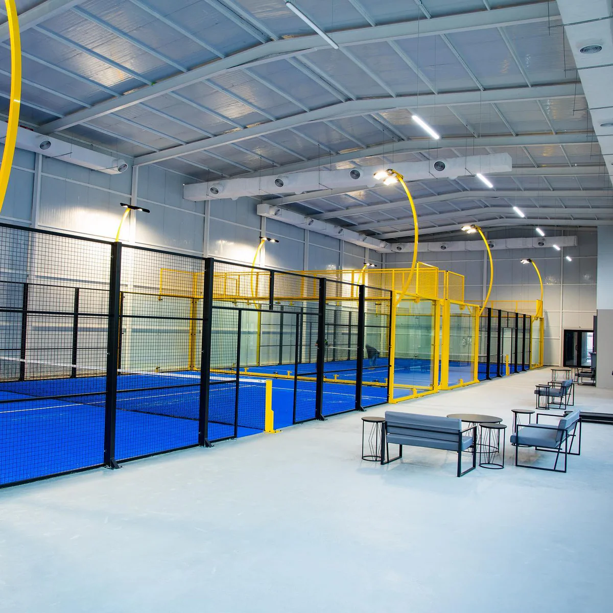 The Padel DC hall from the lounge: courts in a row under arched floodlights